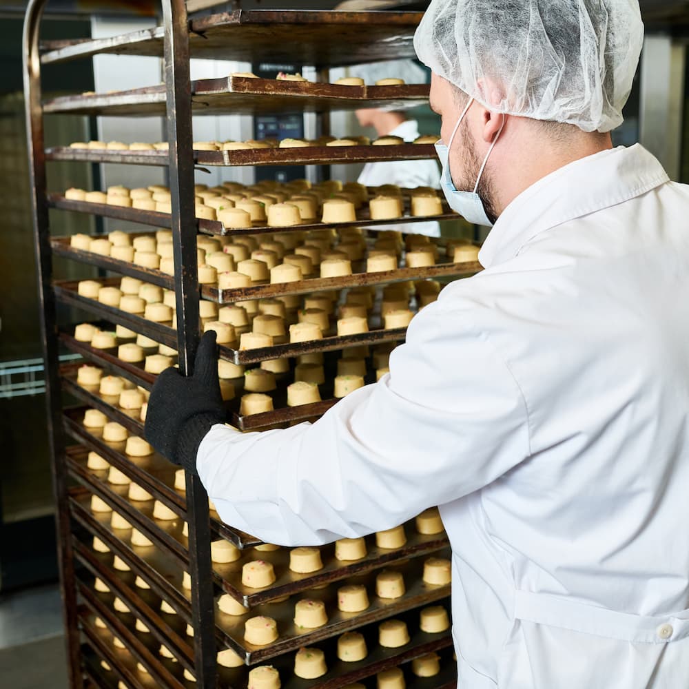 confectionery-factory-worker-pushing-trays-rack-wi-QH3TK5S
